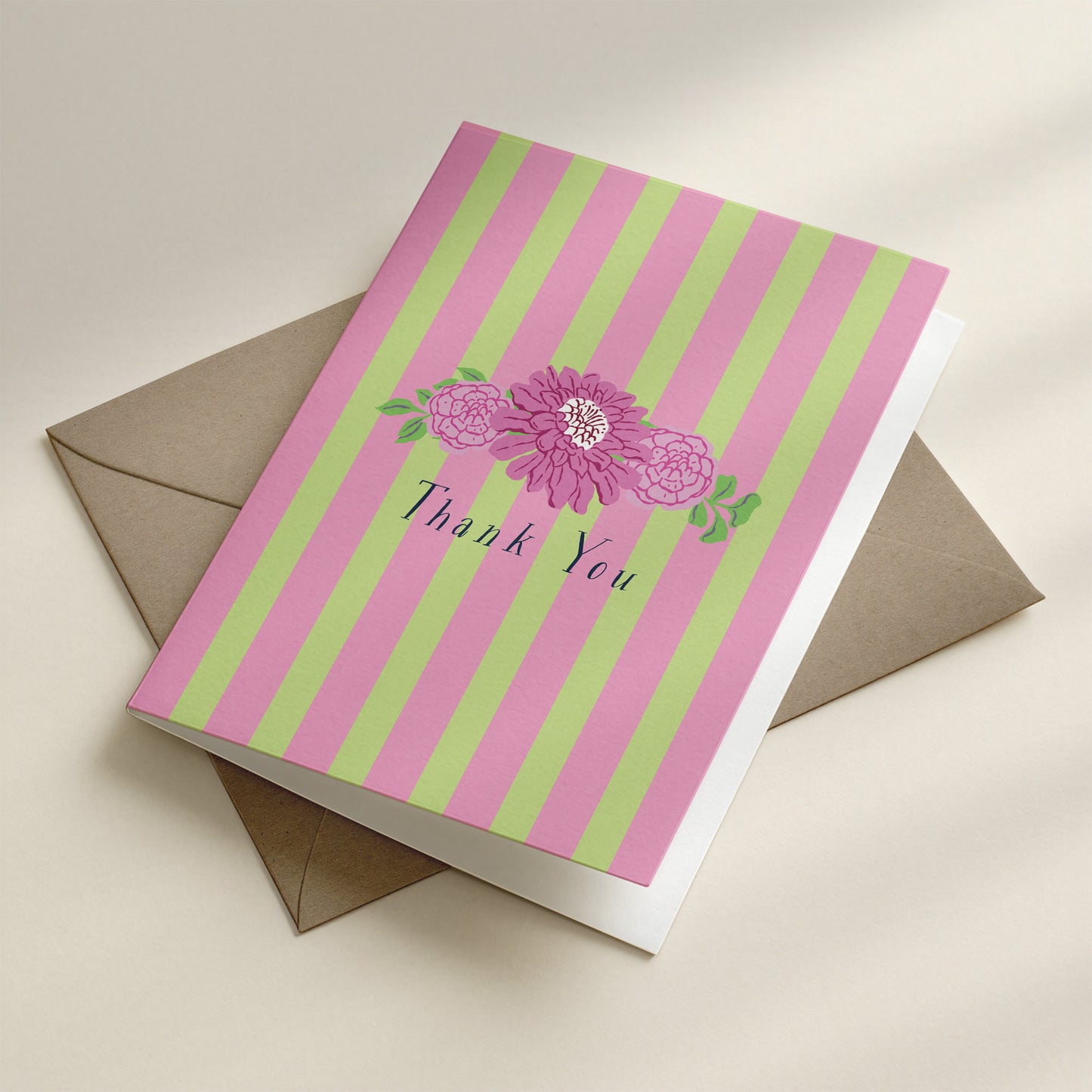 Greeting card with pink and green stripes and a flower design, placed on a beige envelope.