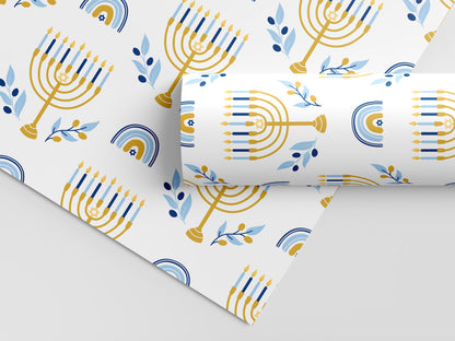 Hanukkah wrapping paper with gold menorahs, blue candles, olive branches, and Stars of David on white.